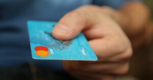 A close-up shot of a hand offering a blue debit card for payment.